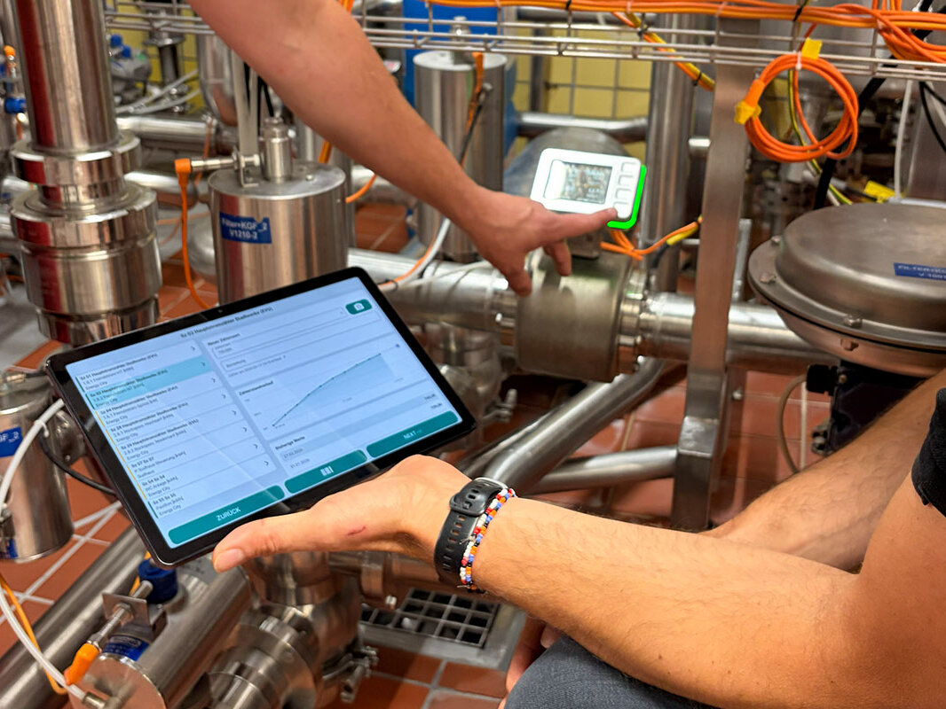 Digitales Energiemanagement in der Brauerei: Eine Person pr&uuml;ft Messwerte an Edelstahlrohren mit Messger&auml;t und Tablet.