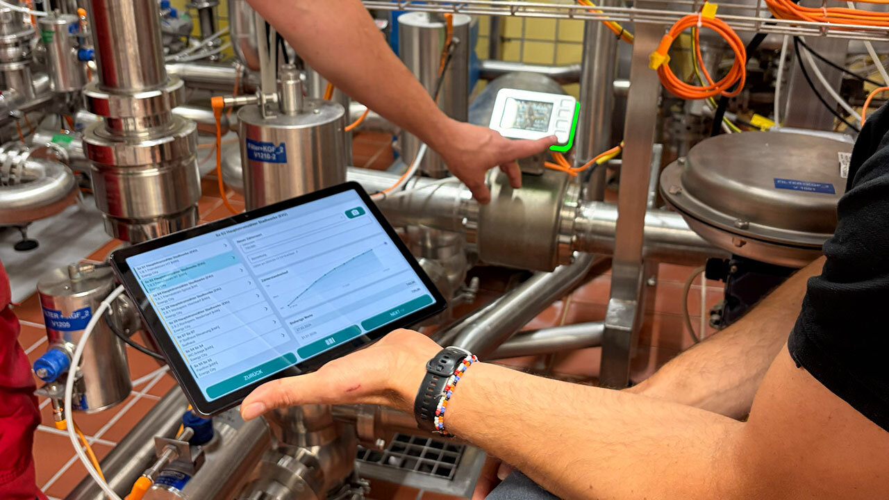 Digitales Energiemanagement in der Brauerei: Eine Person prüft Messwerte an Edelstahlrohren mit Messgerät und Tablet.